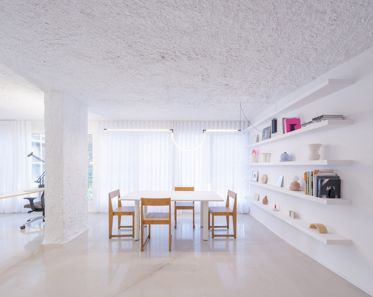 Open-plan dining area with timber table and chairs beneath a sprayed white ceiling and cylindrical column