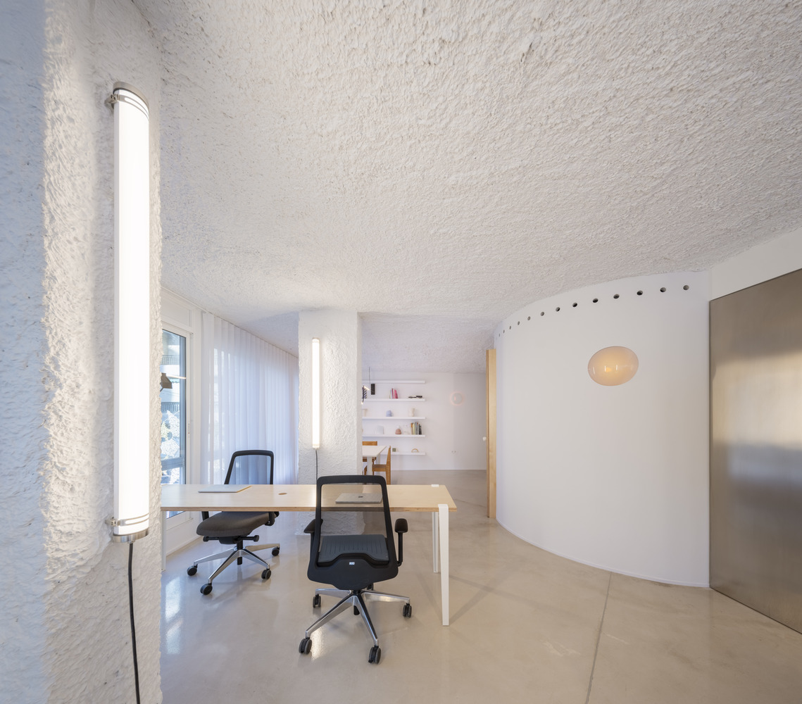 Office desk with two chairs under a tubular light fixture mounted on the textured wall