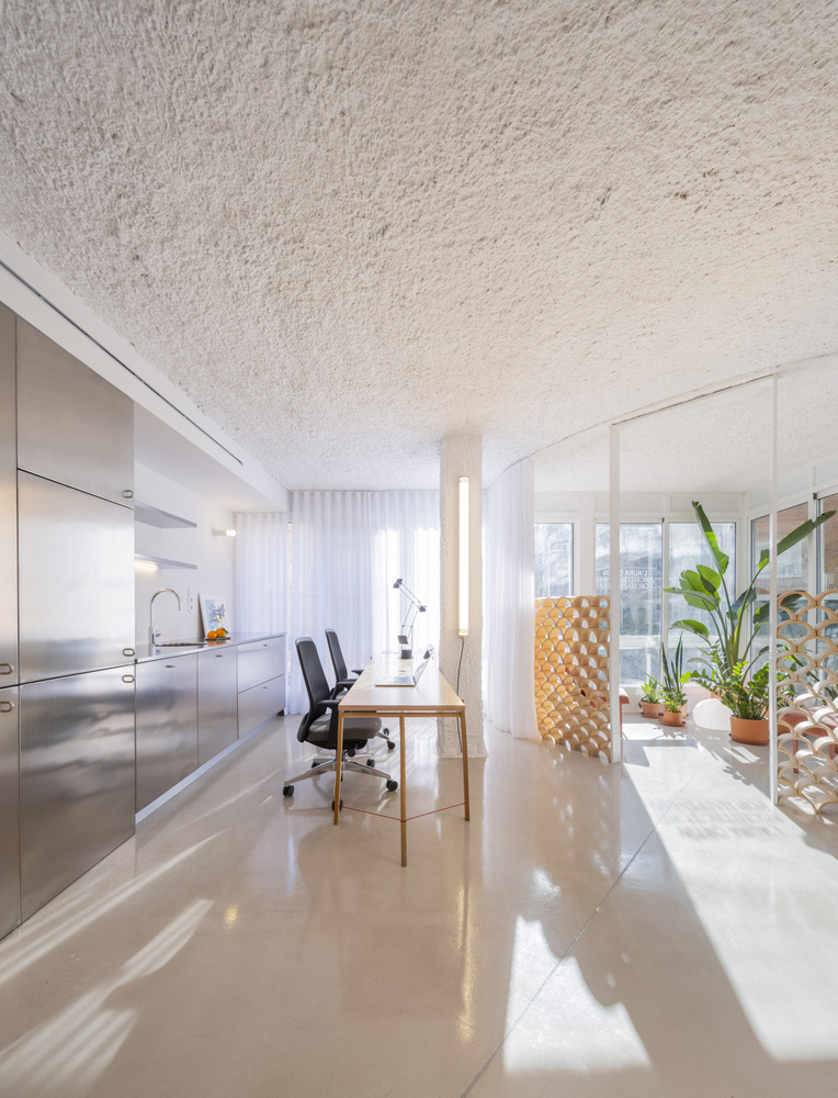 Long view through the polished floor showing kitchenette, workspace, and screened balcony in daylight