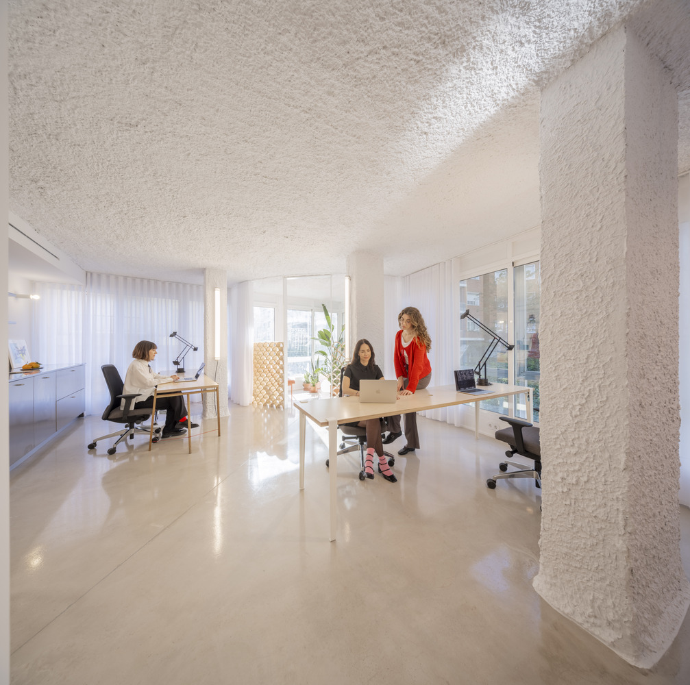Open workspace with polished concrete floor, white textured ceiling and columns, and three people at desks