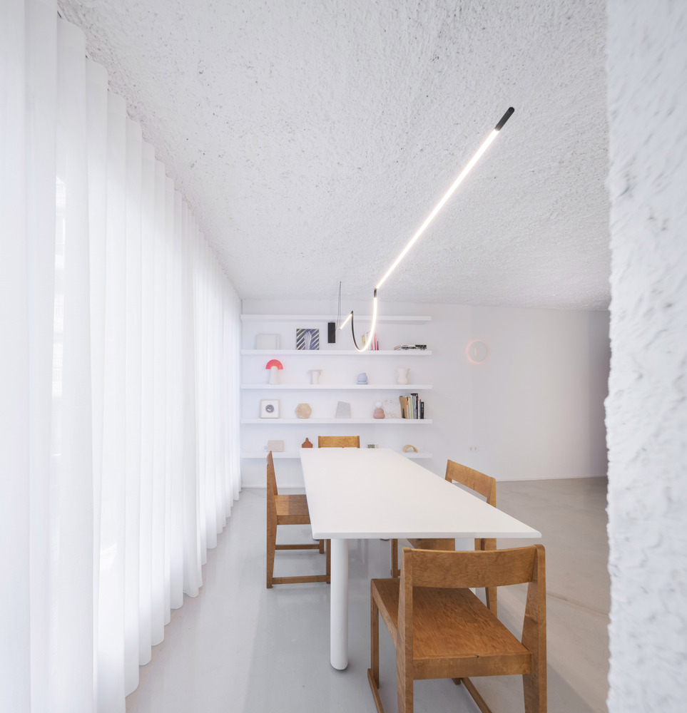 Meeting room with long white table, timber chairs, and articulated lighting fixture under textured vaulted ceiling
