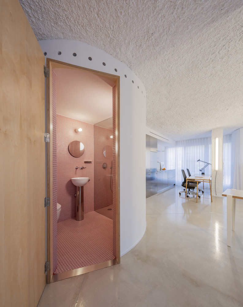 Arched doorway framing pink tiled bathroom pod set within white textured walls and blonde timber joinery