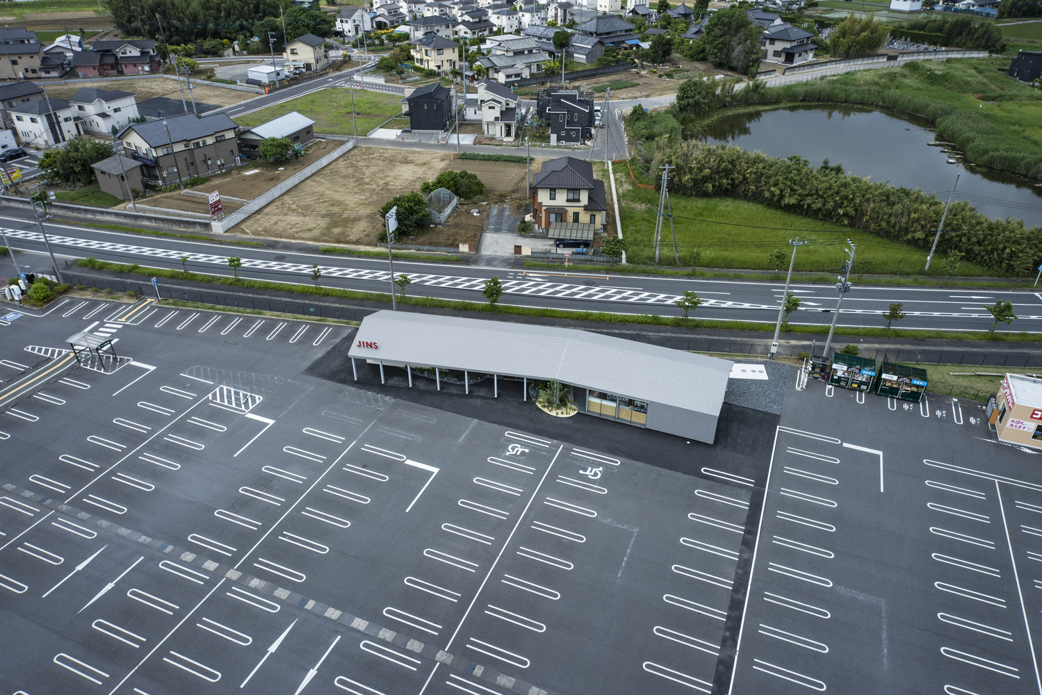 Aerial view of the single-story pavilion with white roof in a parking lot beside residential houses
