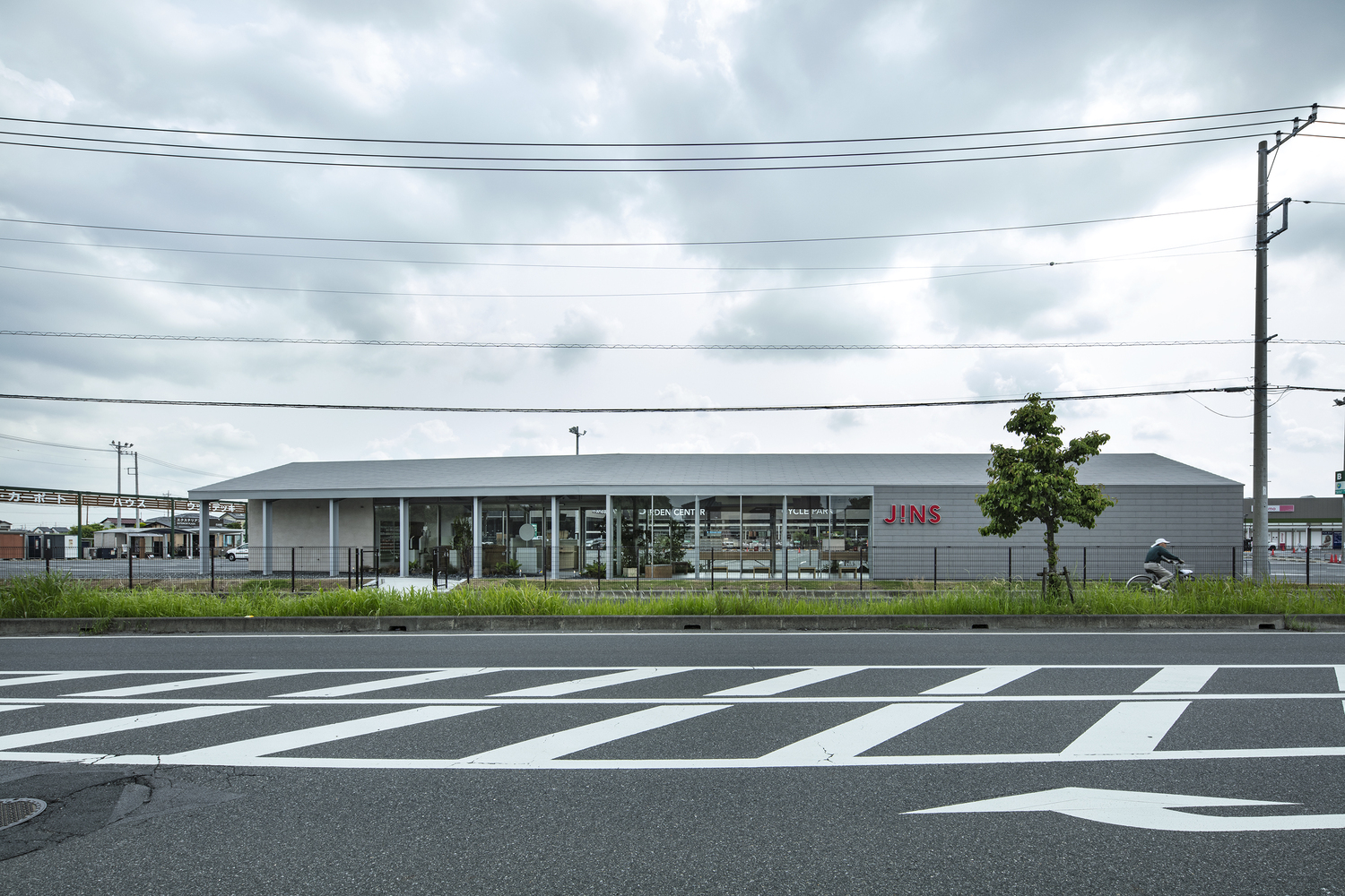 Street view of the low horizontal volume with glazed facade and striped pedestrian crossing in foreground