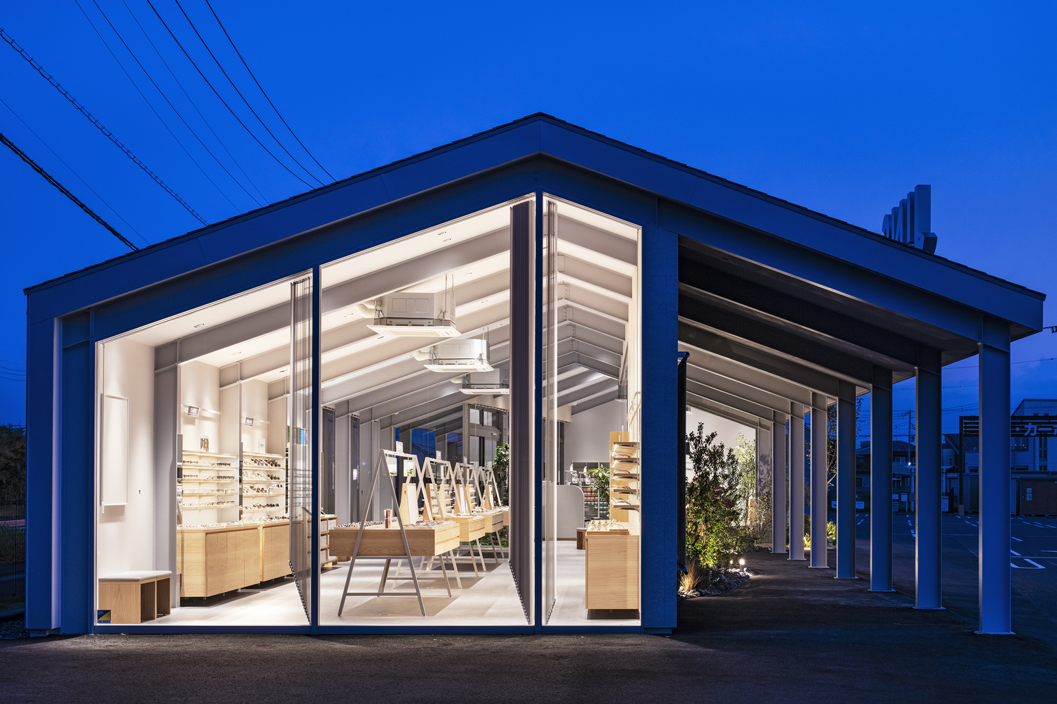 Fully opened glazed corner with exposed ceiling rafters and interior lighting at dusk