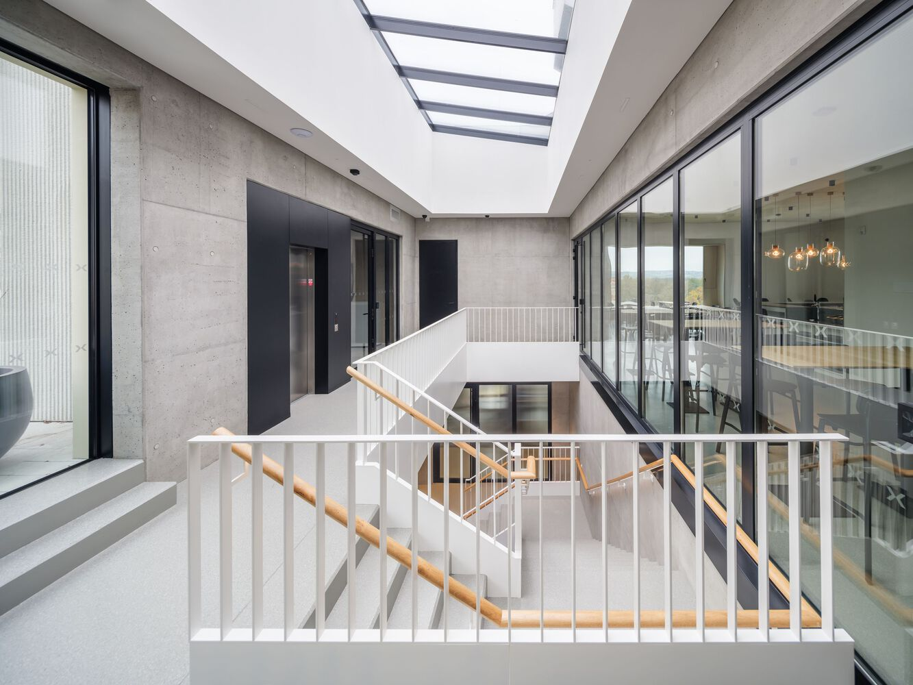 Interior stairwell with white metal railings and timber handrail beneath a slatted skylight