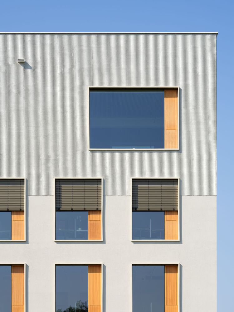 Facade detail showing corrugated metal cladding above smooth render with timber-lined window openings and exterior blinds