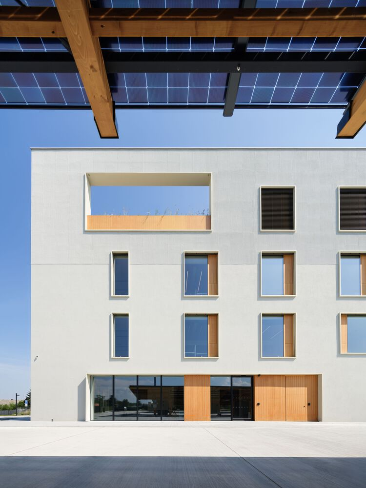 Main facade with timber beam canopy supporting solar panels above a ground-floor glazed entry and timber doors