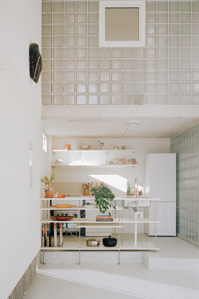 Grid skylight above freestanding kitchen shelving unit with pale tile wall and vaulted plywood ceiling beyond
