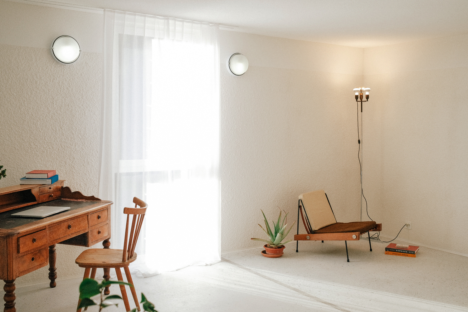 Sparsely furnished white room with sheer curtained doorway and circular wall-mounted lights in soft natural light