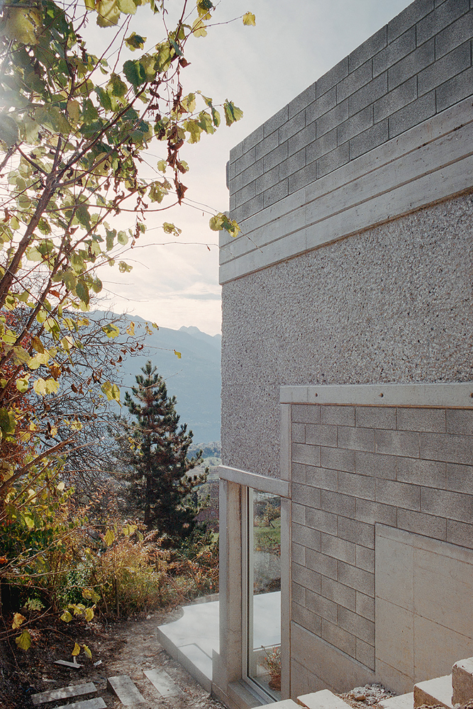 Concrete block wall corner with textured stucco band beside grape vine and distant mountain view at dusk