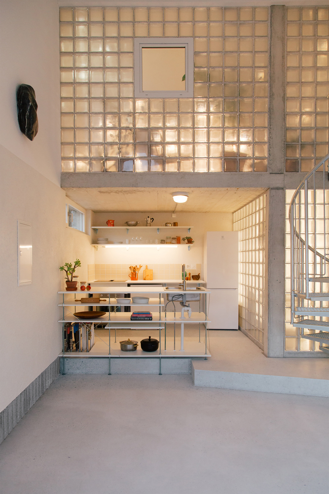 Double-height interior with translucent glass block mezzanine above an open kitchen with metal shelving