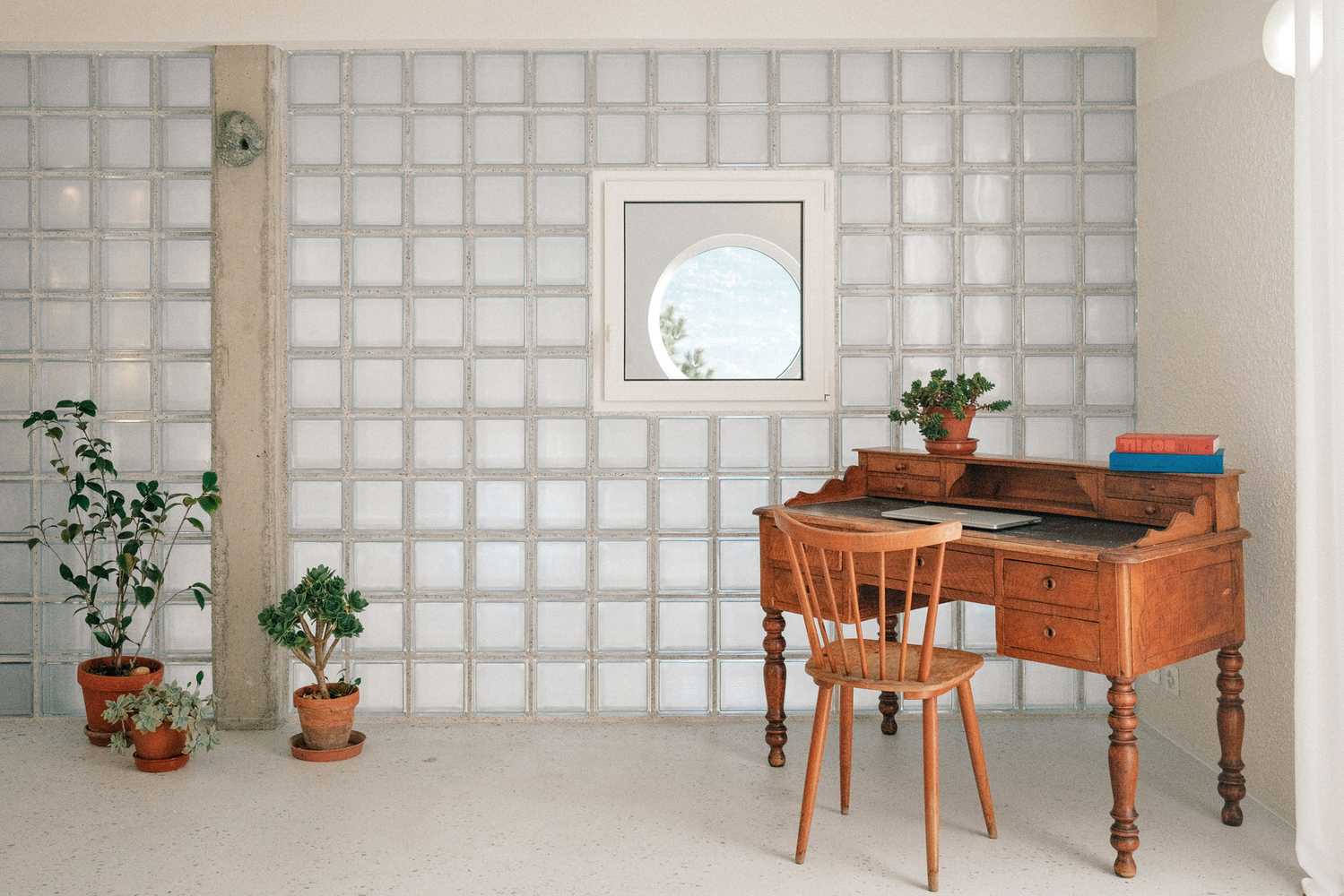 Glass block wall with circular window opening and antique wooden desk with potted plants