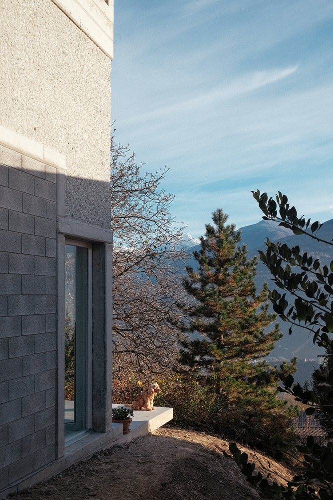 Exterior corner showing textured plaster and grey block walls with a glass door opening to mountain views