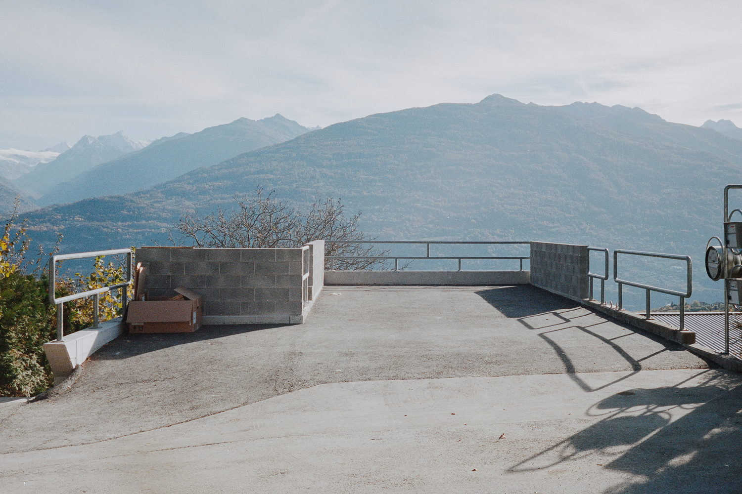 Roof terrace with metal railings and concrete parapet overlooking distant mountain range in afternoon light