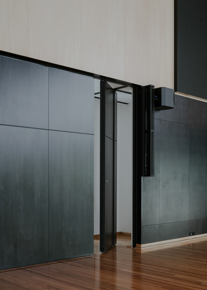 Black folding partition door opening in the dark paneled wall beside timber flooring