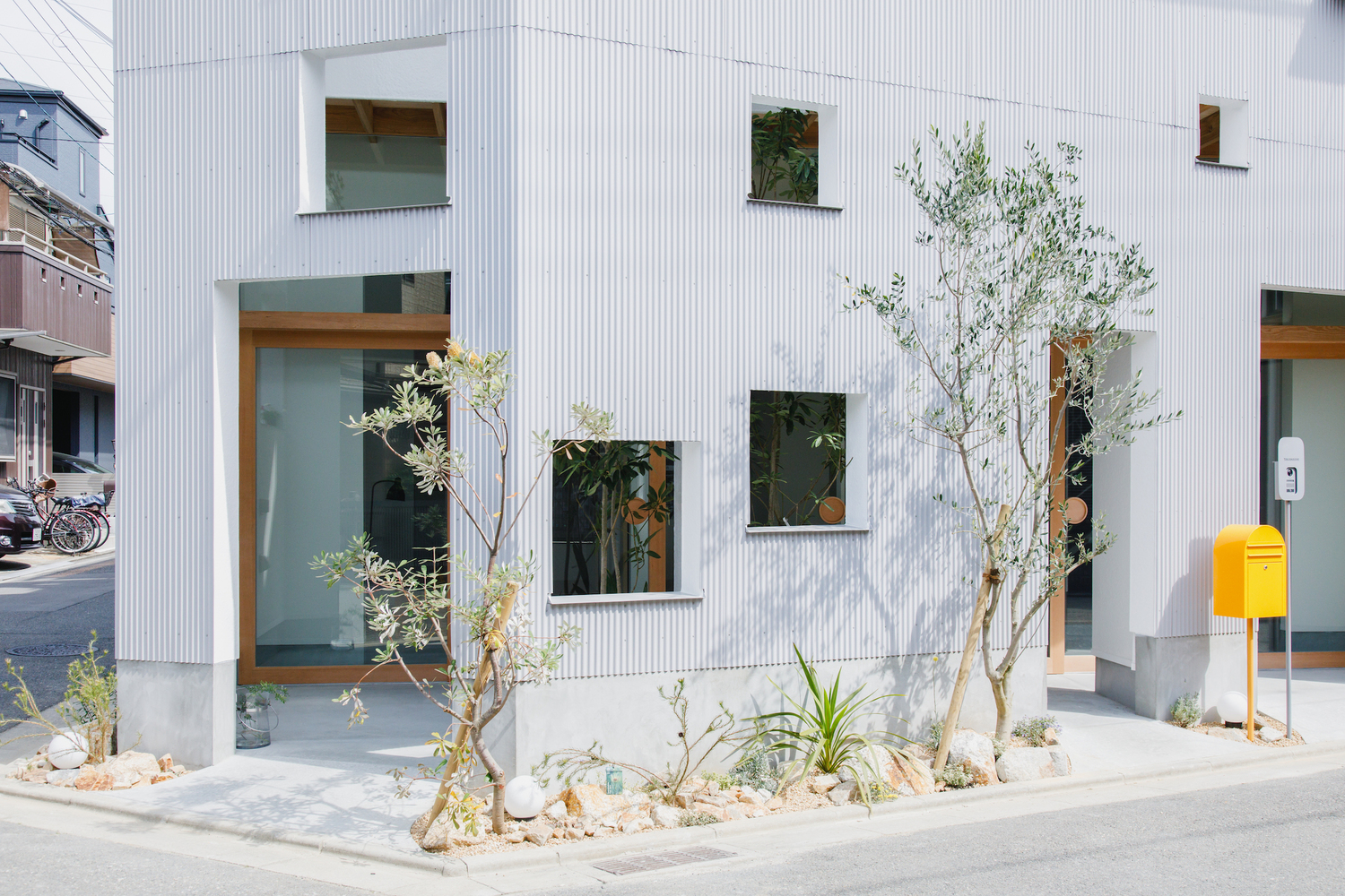 Entry facade with timber-framed openings and young olive trees in a gravel bed