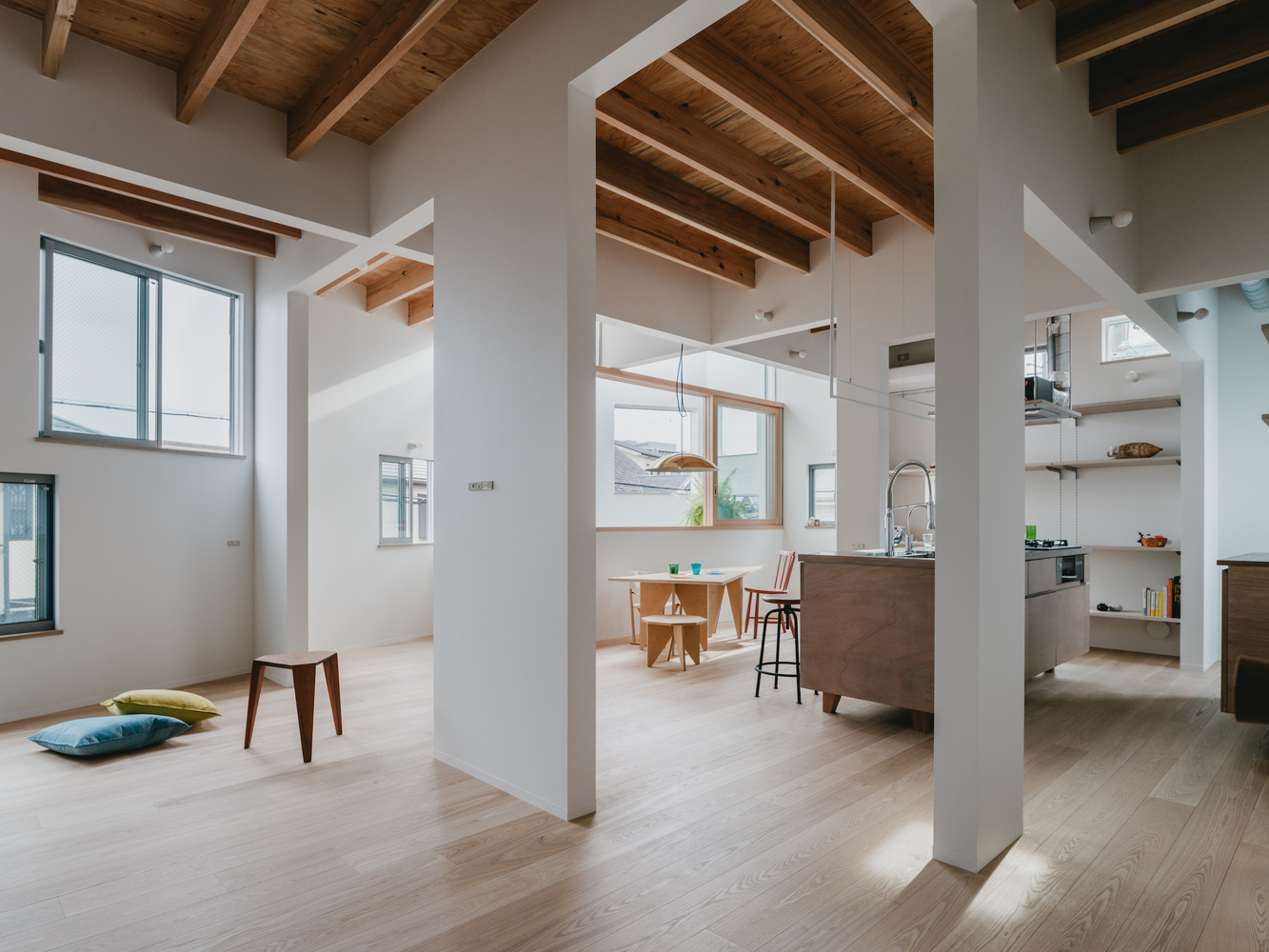 Open-plan living space with exposed timber ceiling joists and white columns separating kitchen and dining areas