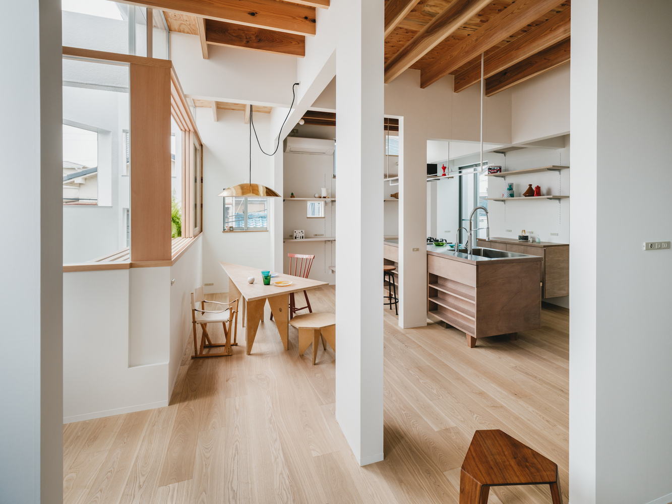 View through white columns connecting the dining area with timber table to the kitchen with island