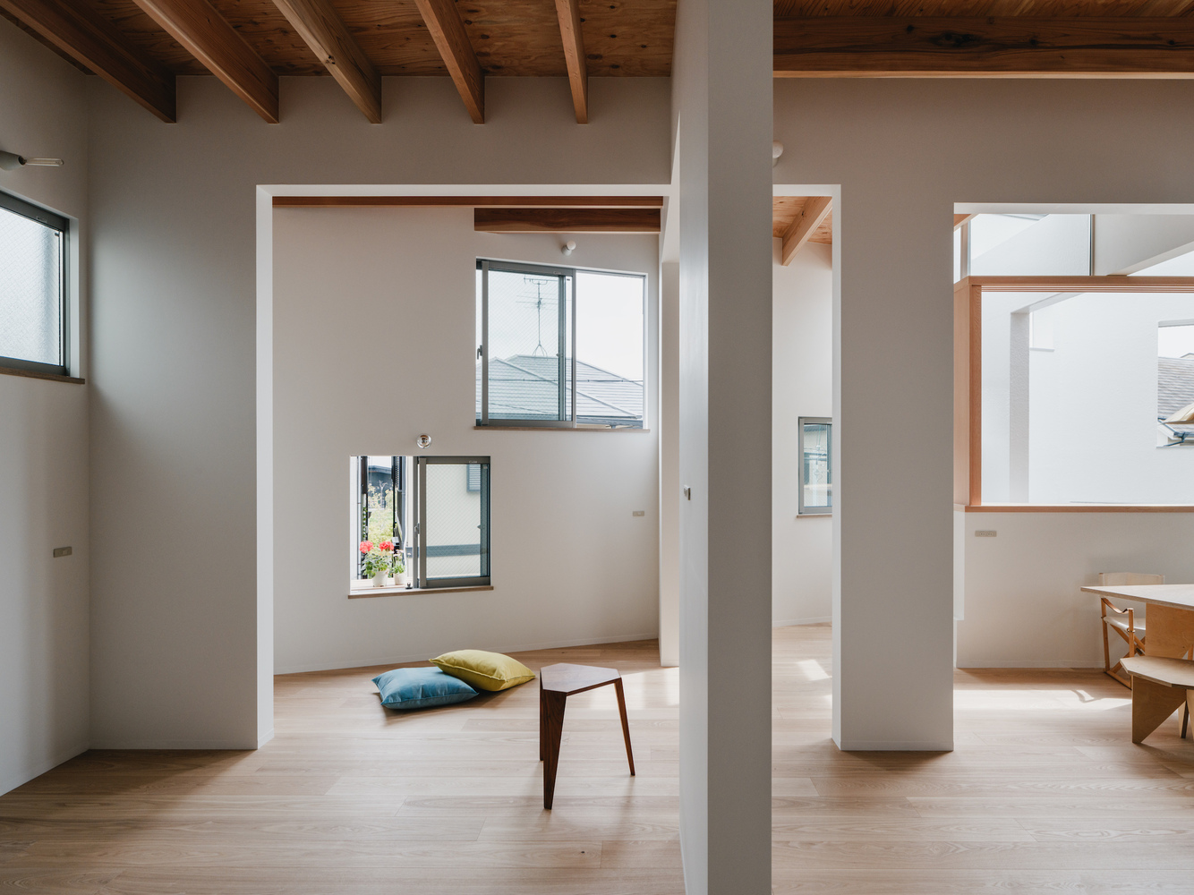 Layered interior rooms framed by white portals with timber ceiling beams and pale flooring