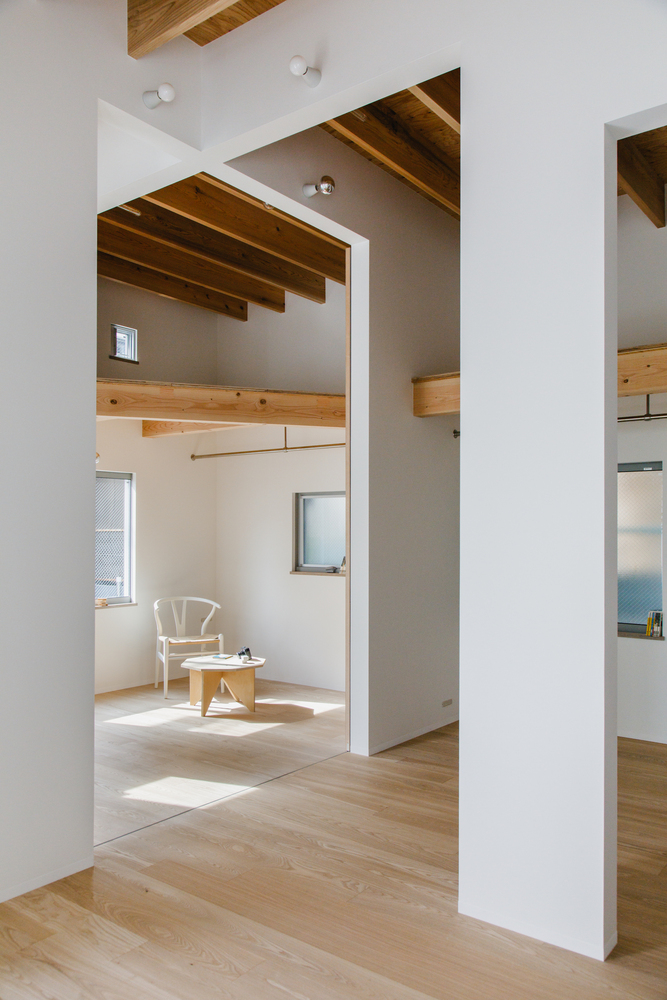 Interior view through offset doorways showing timber ceiling structure and seated furniture in sunlight