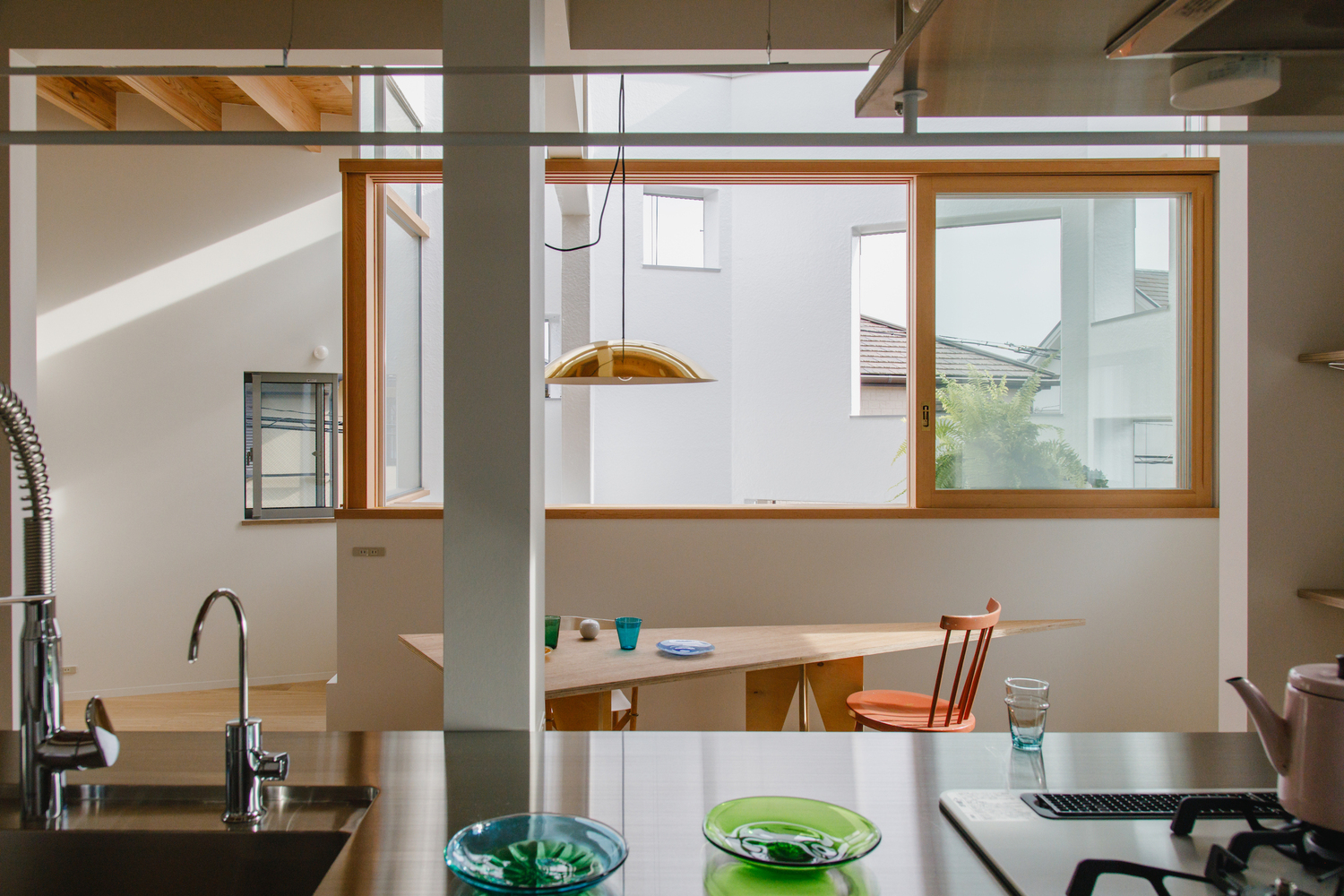 Kitchen counter with green glass bowls facing dining table and sliding wood-framed window