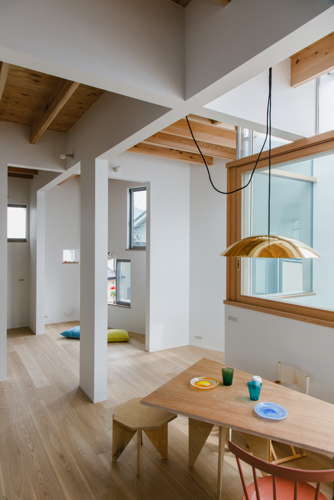 Double-height dining space with exposed timber ceiling joists and a brass pendant light over a wooden table