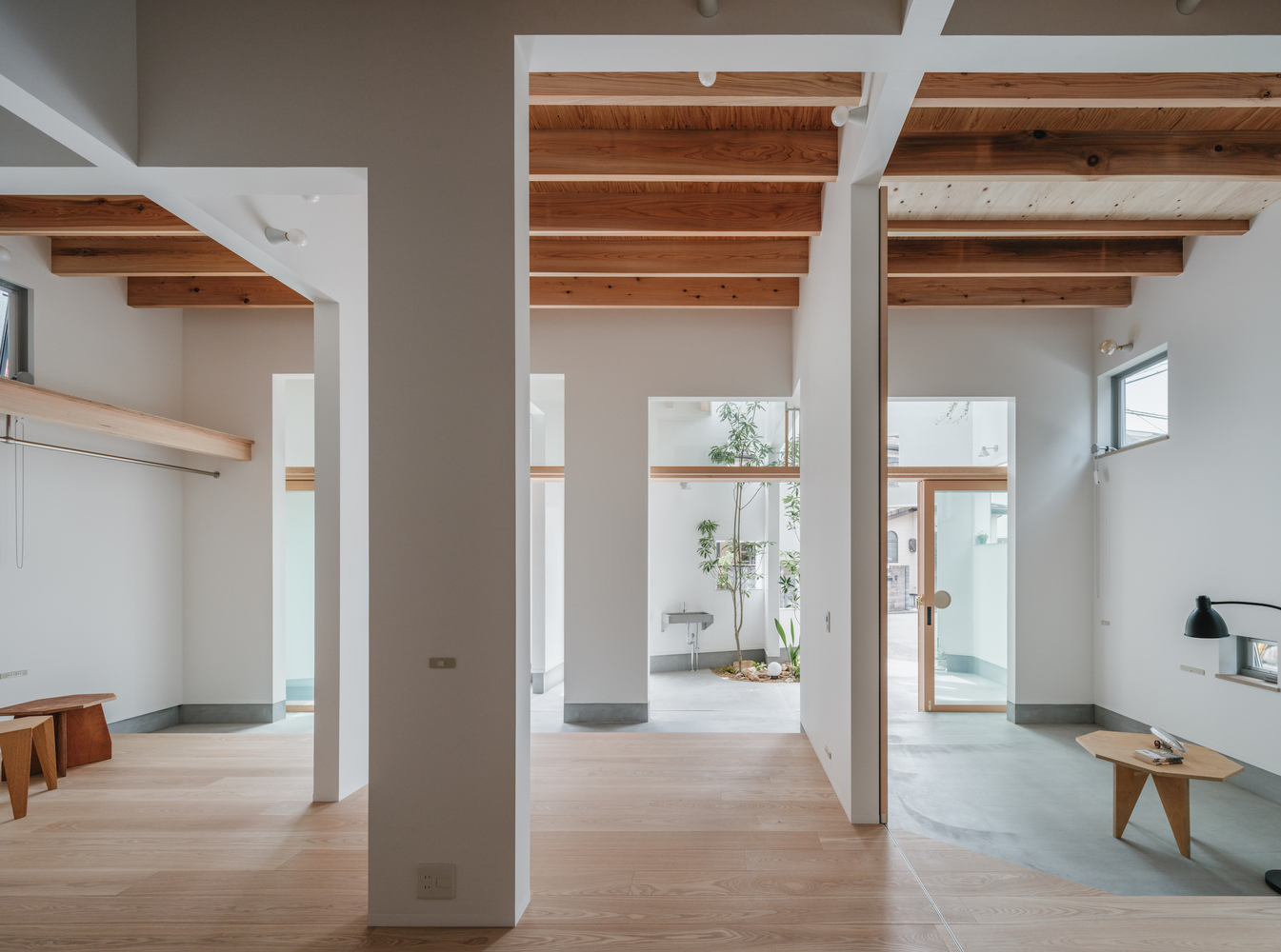 Open plan interior with exposed timber beams and white structural columns separating rooms with timber and concrete floors