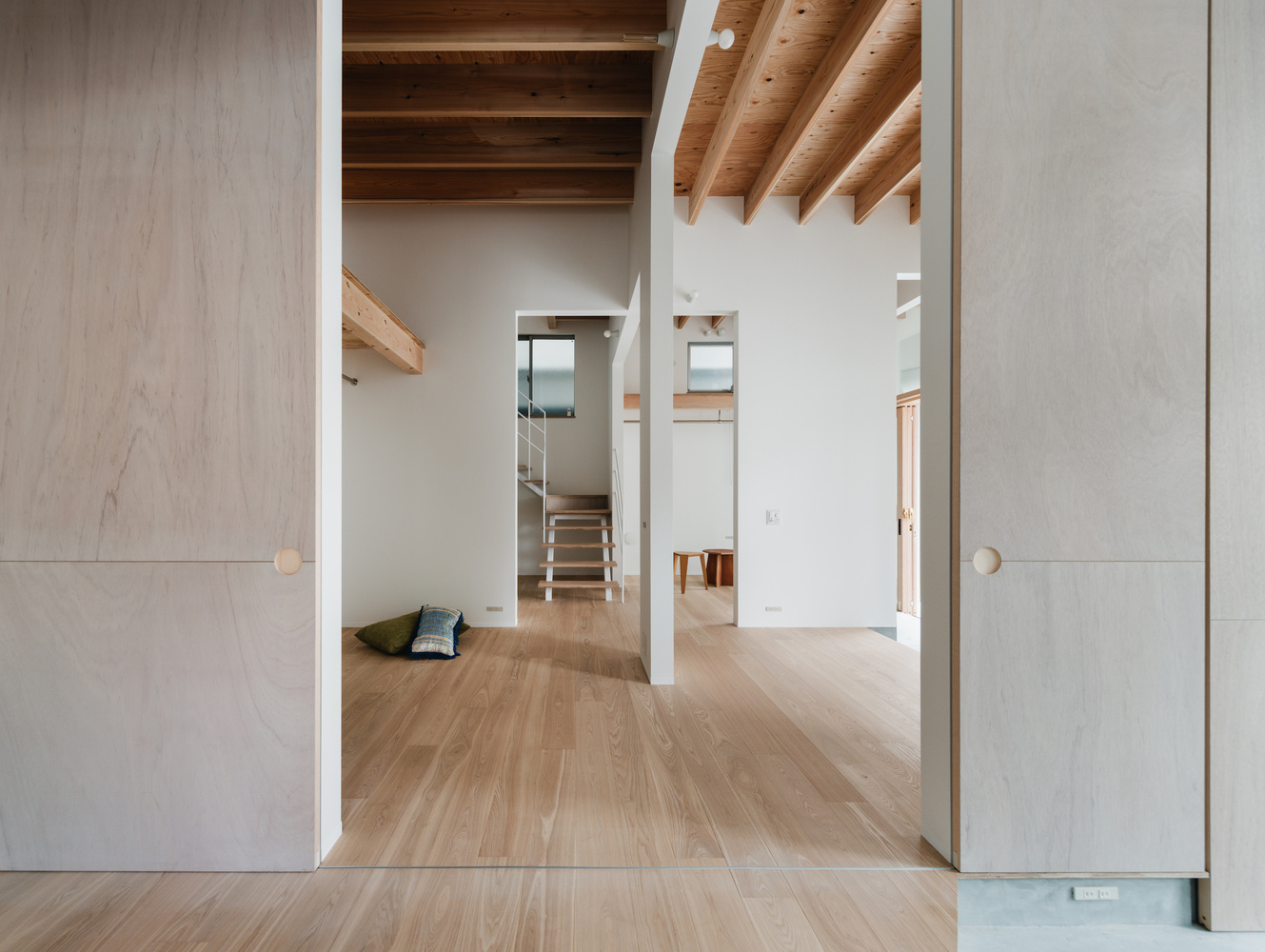 Sliding door threshold between pale timber flooring and white walls beneath exposed timber ceiling joists