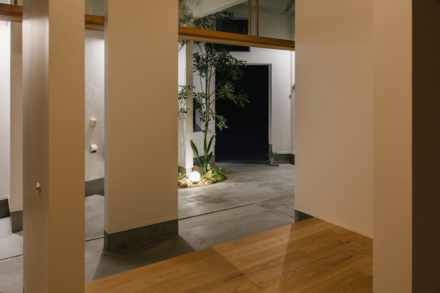 Interior threshold between timber floor and polished concrete with planted courtyard visible at dusk