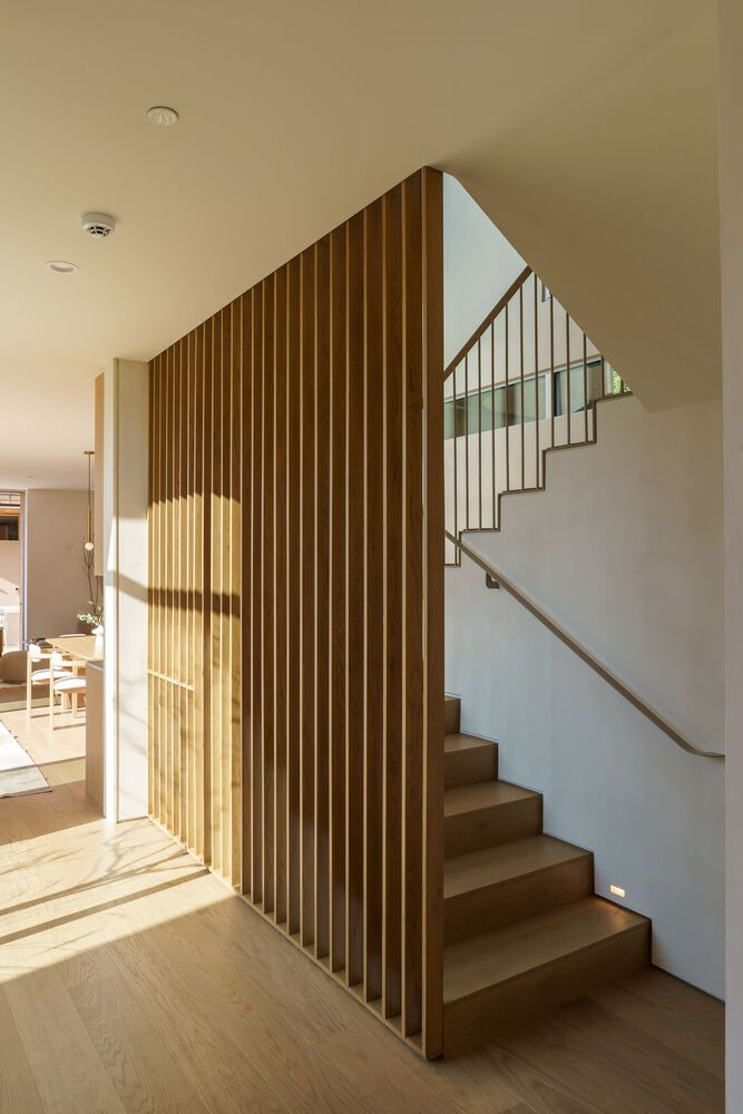 Interior staircase with vertical timber slat screen and white wall with sunlight streaming through