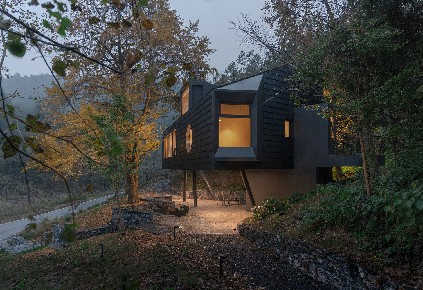 Elevated structure on steel columns with illuminated windows glowing at dusk among sparse trees
