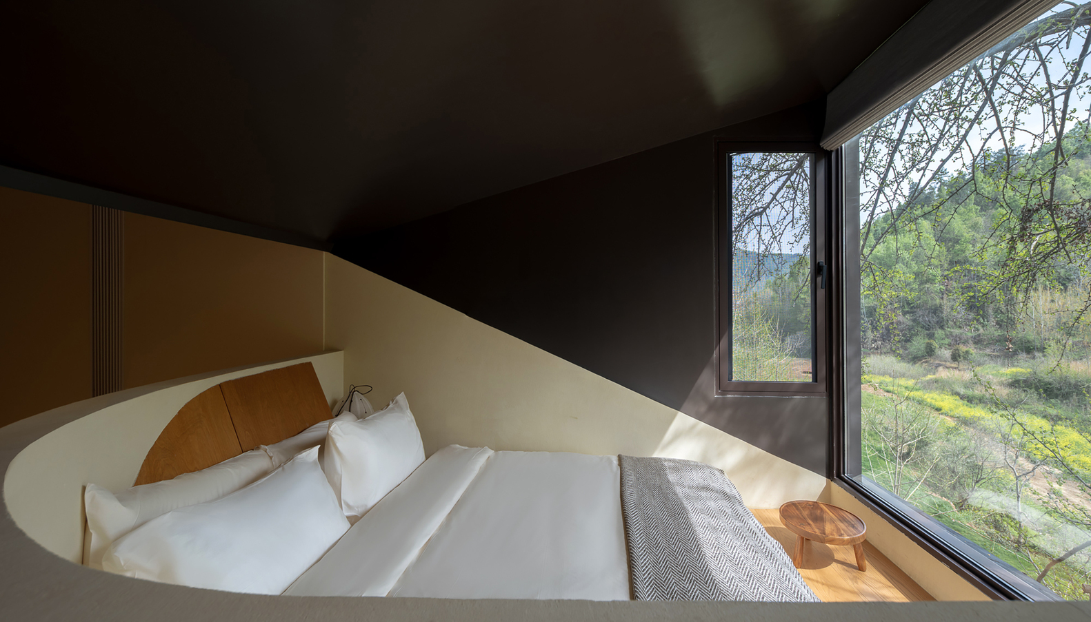 Bedroom with curved plaster walls and corner window framing the green hillside beyond