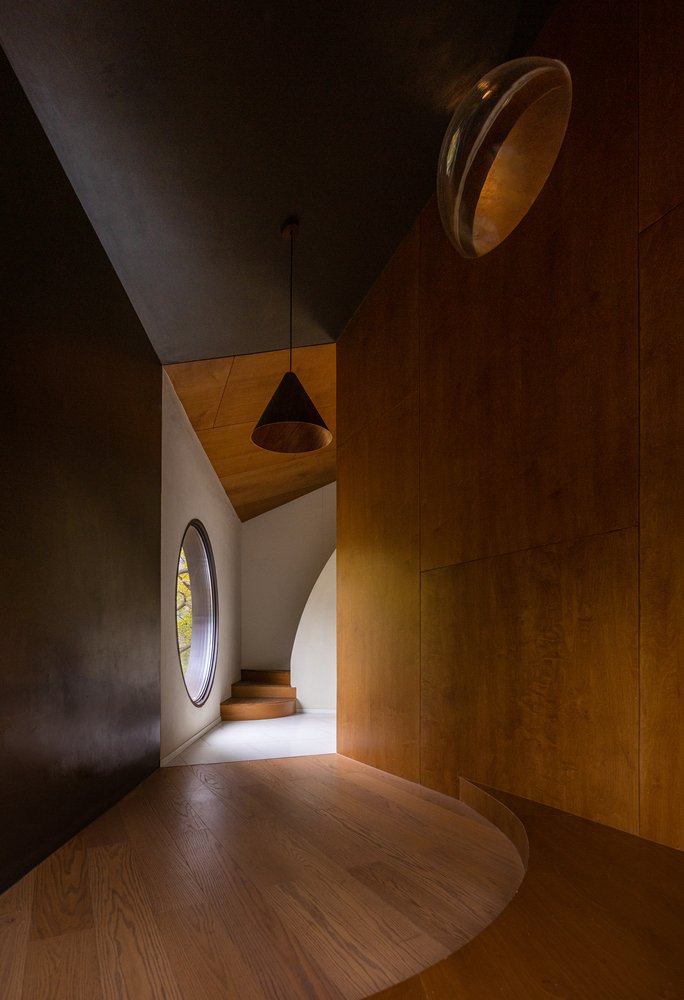 Curved hallway with dark plaster walls and circular windows admitting daylight from above