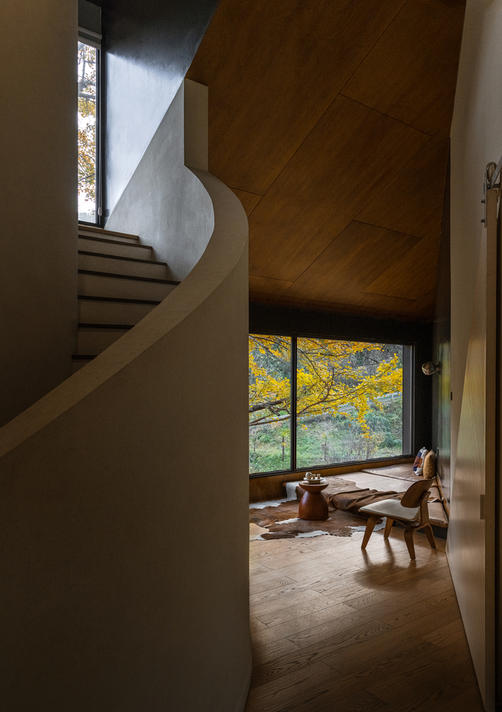 Curved staircase and wood-paneled ceiling overlooking a seating area with autumn foliage visible through the window