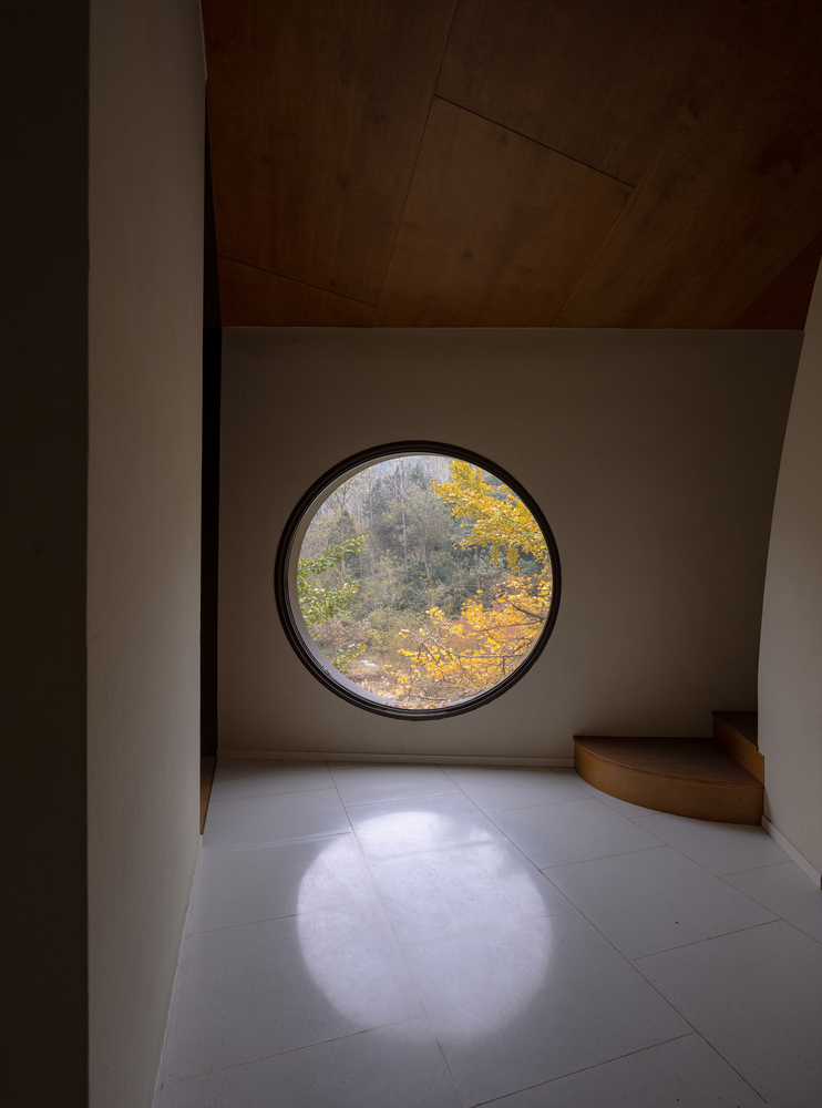 Circular window framing autumn trees with sunlight pooling on the pale floor below
