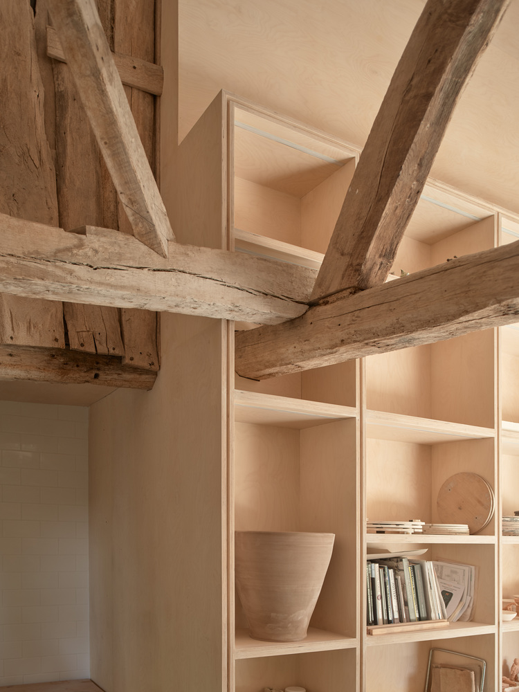 Corner detail showing exposed timber beams intersecting with built-in plywood shelving holding ceramic objects