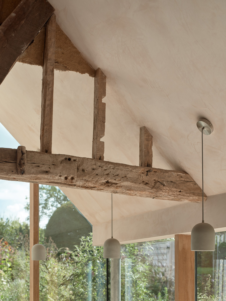 Vaulted ceiling with exposed timber beams and pendant lights above glazed openings to garden
