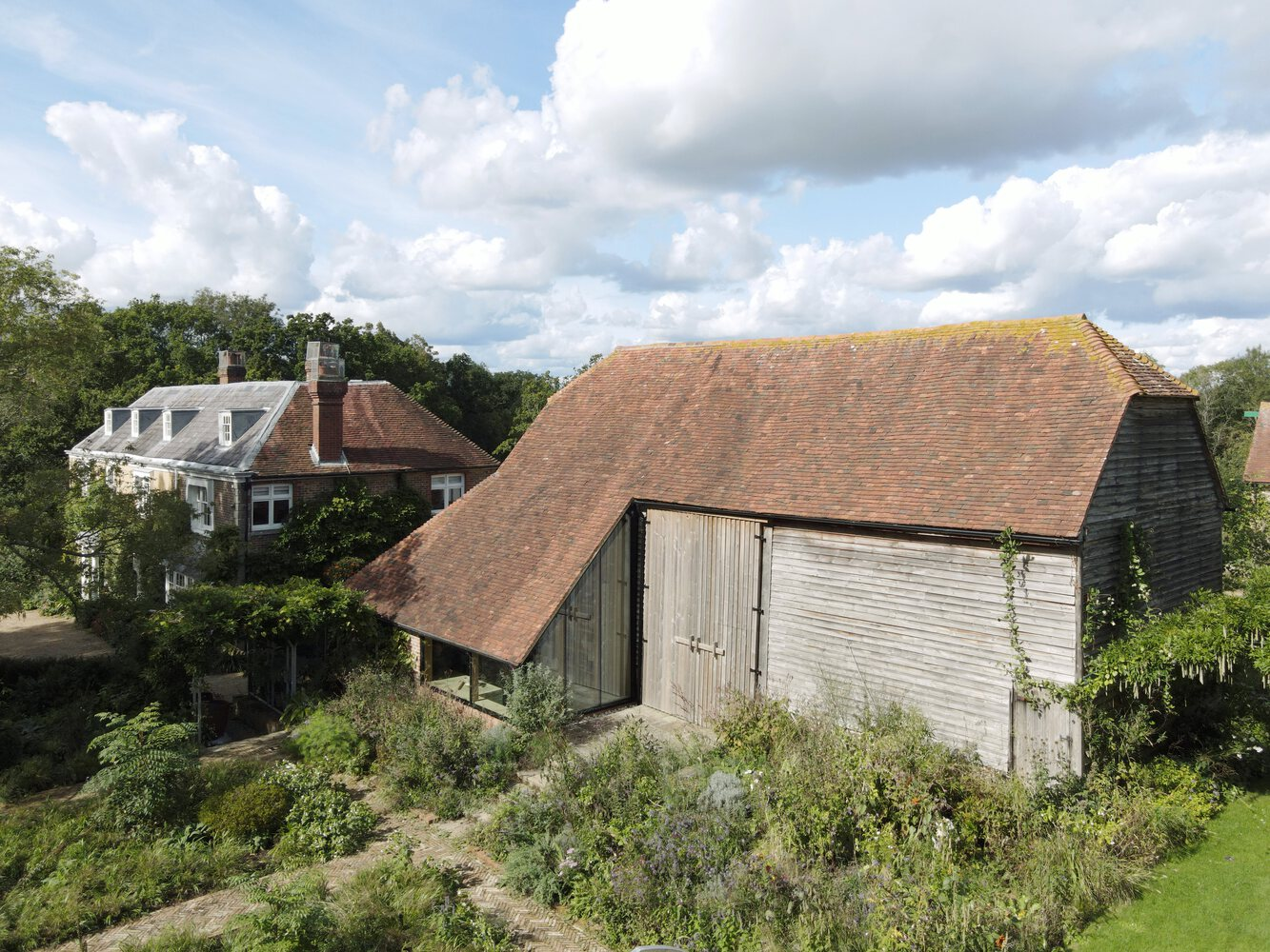 Aerial view of the tiled barn roof and glass extension surrounded by garden planting