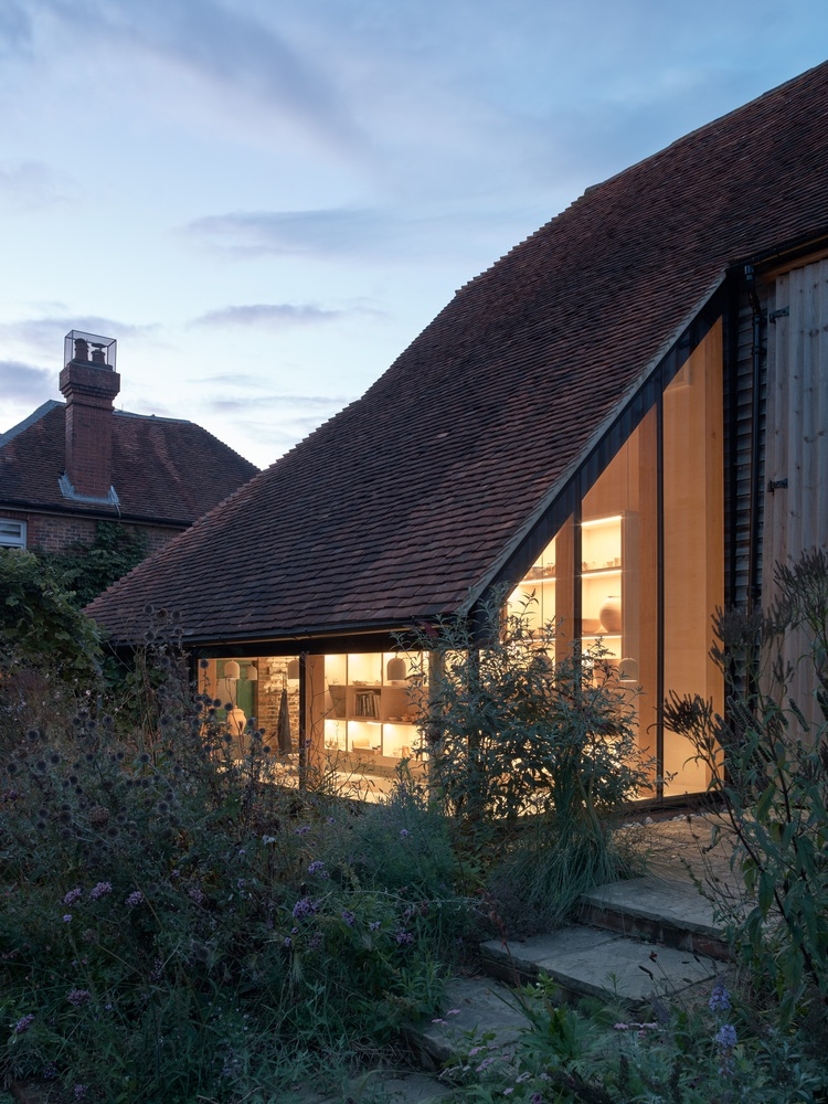 Garden view of the tiled pitched roof and glazed gable at dusk with interior lights illuminated