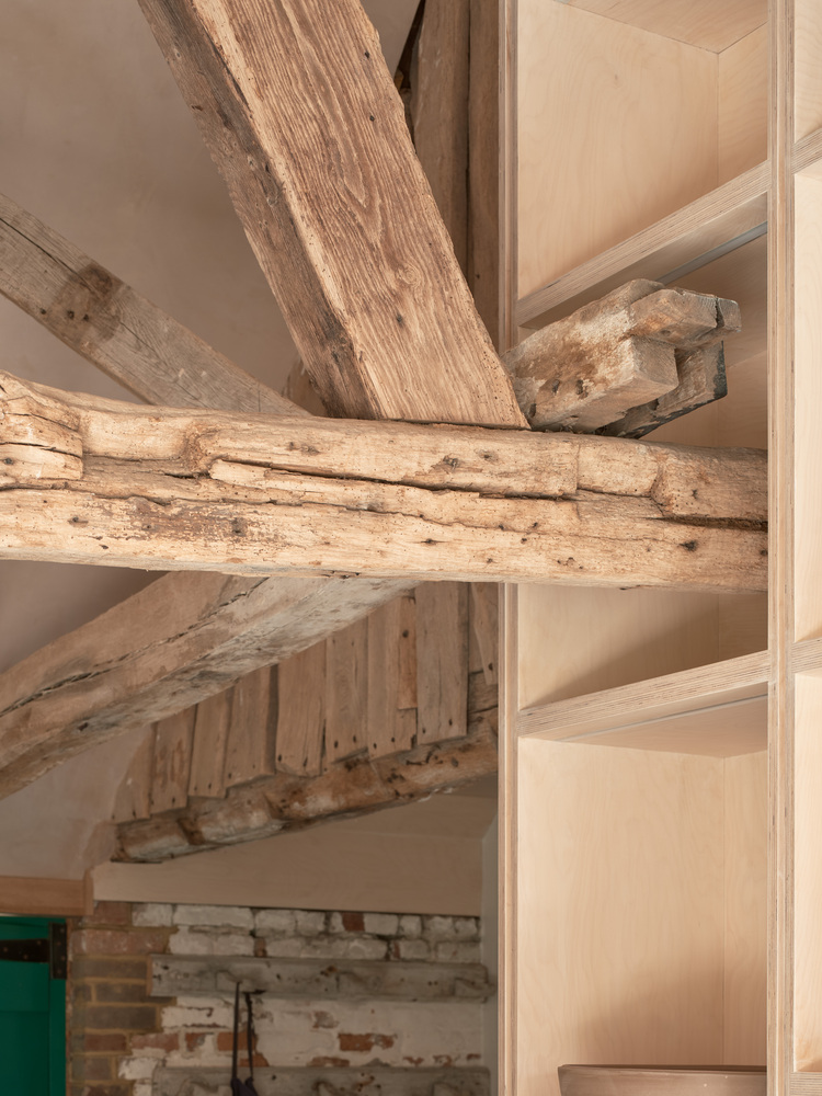 Close-up of exposed timber beam joints intersecting with new timber framing and painted brick wall