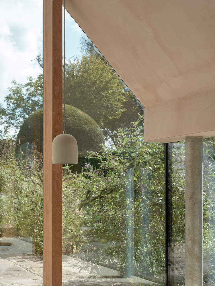 Triangular timber-framed window opening onto a garden with rounded topiary and grasses