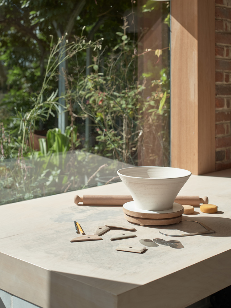 Close-up of pale stone countertop with bowl and timber trivet in dappled sunlight