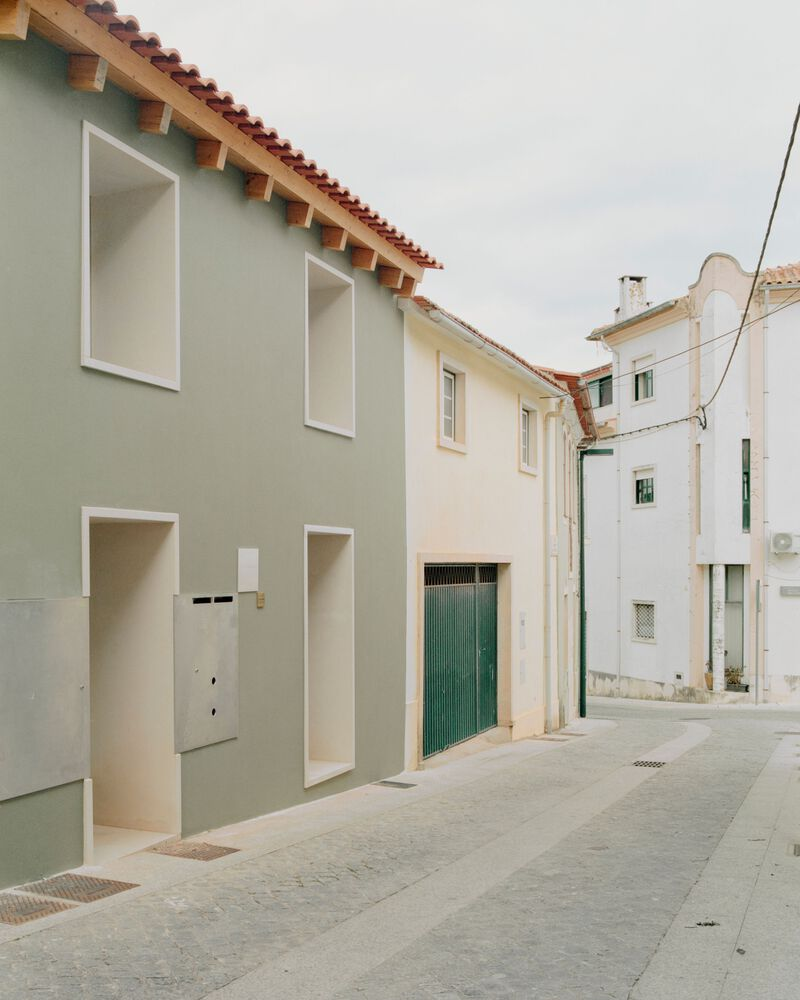 Street facade with deep recessed openings in sage-green render and red clay tile roof