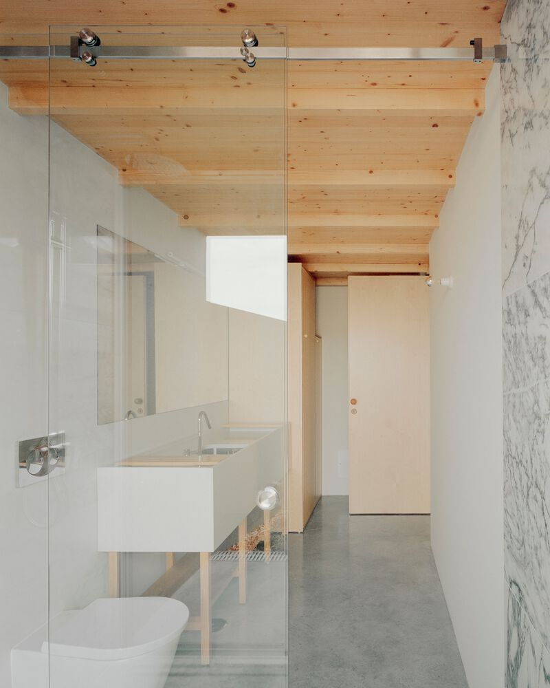 Bathroom with exposed timber ceiling beams and glass shower partition overlooking polished concrete floors