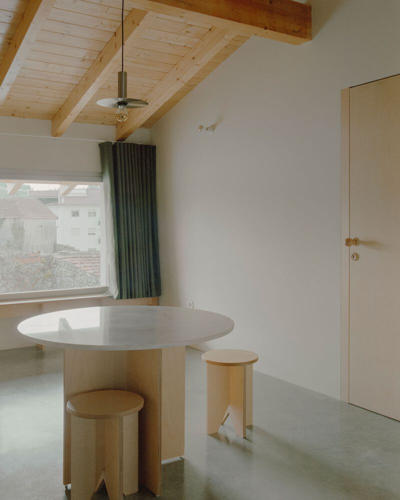 Round concrete dining table with timber stools beneath a pitched timber ceiling and pendant light