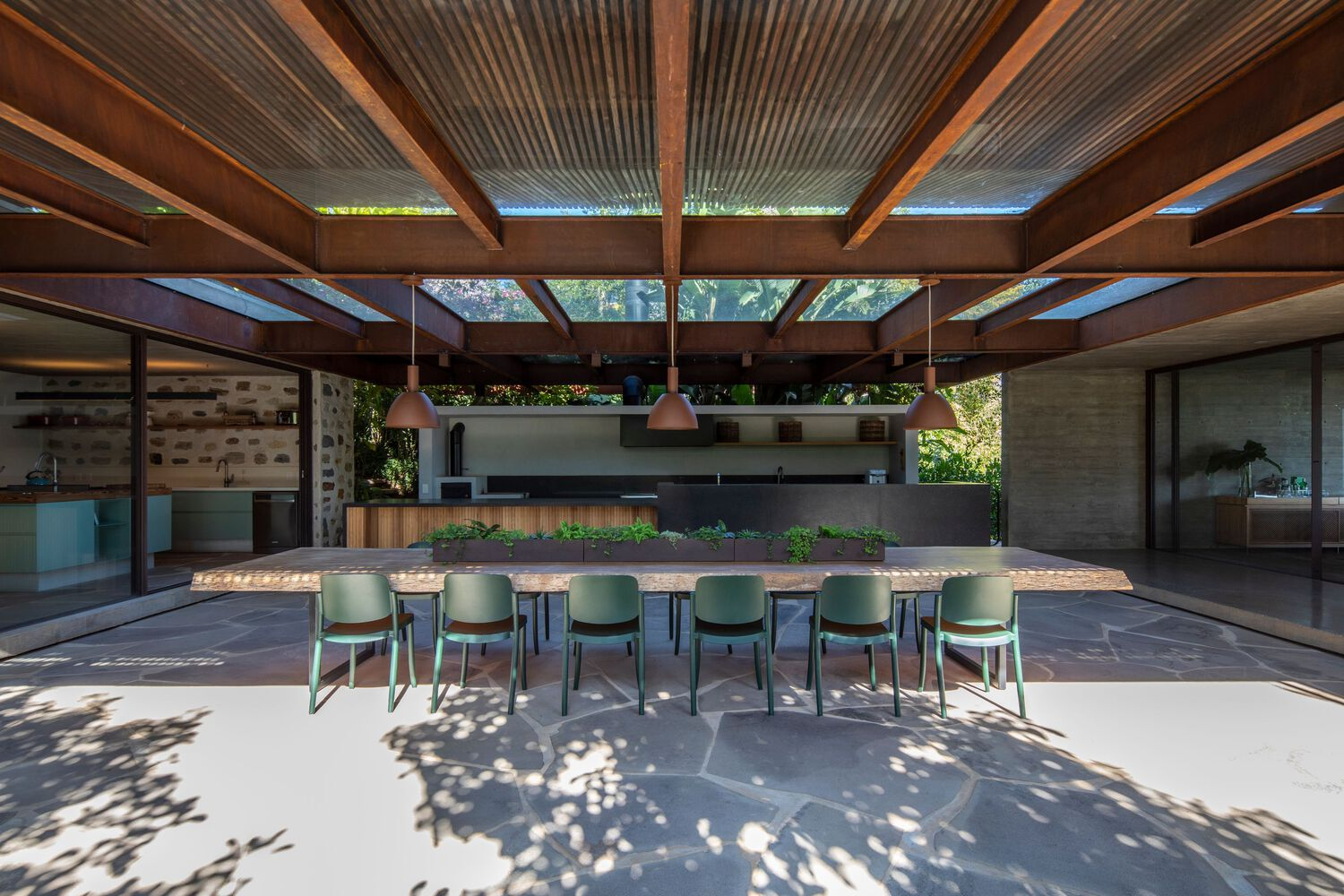 Covered outdoor dining area with exposed timber beams and corrugated metal ceiling panels filtering dappled light