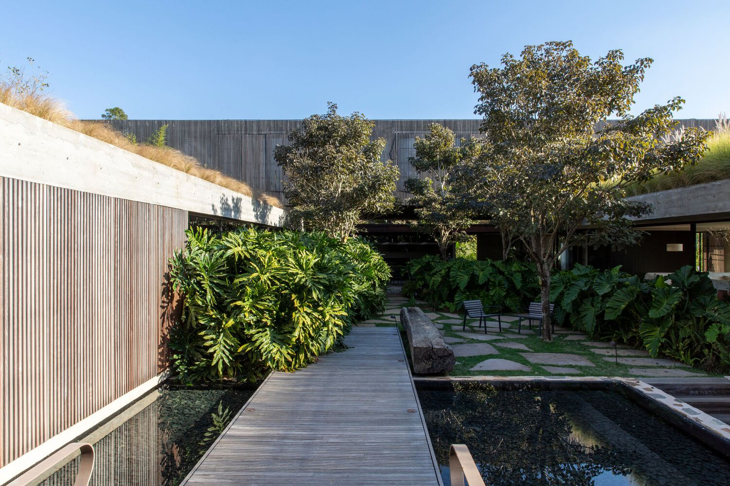 Timber boardwalk crossing a reflecting pool surrounded by stone walls and tropical planting