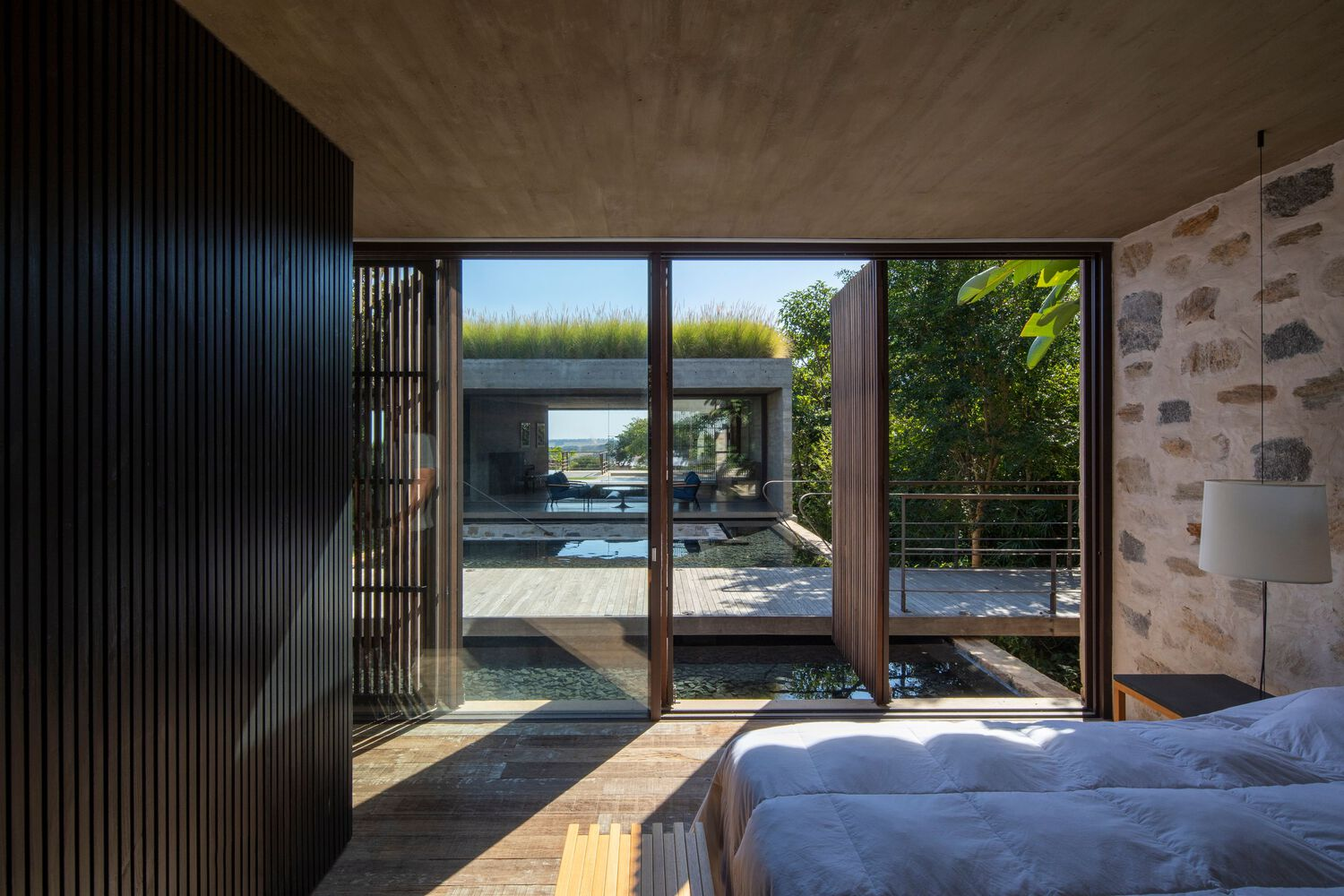 Bedroom with full-height glazing opening to a pool deck framed by vertical timber screens
