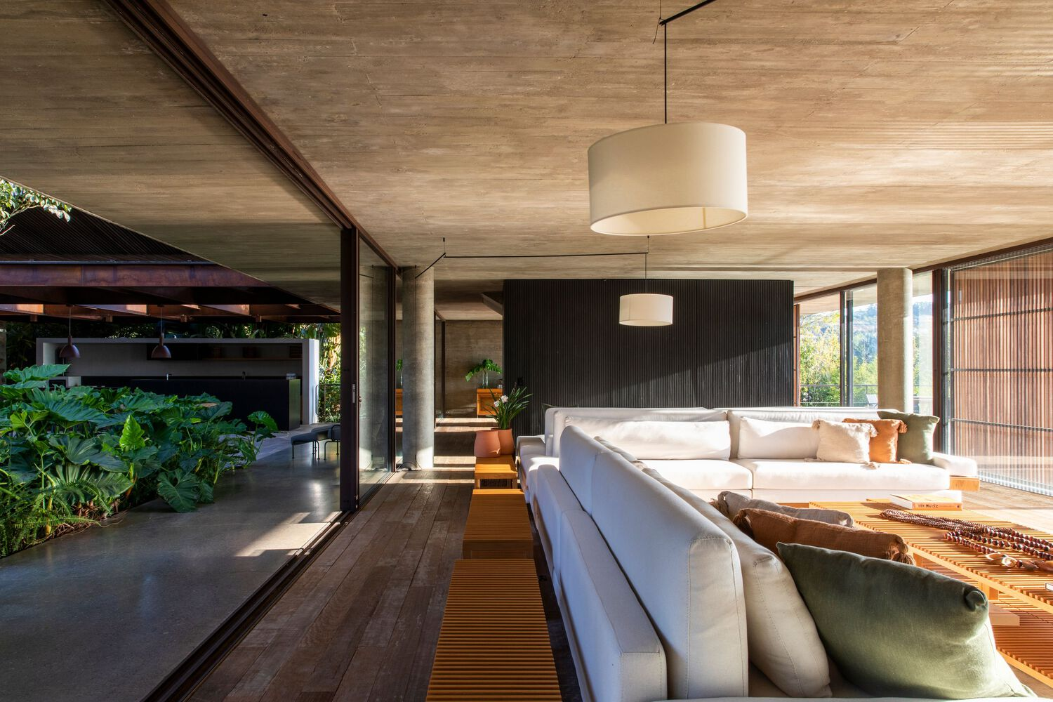 Open-plan living space with timber-lined ceiling and sliding glass walls to planted courtyard at dusk